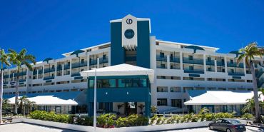 Modern resort building with palm trees under clear blue sky.