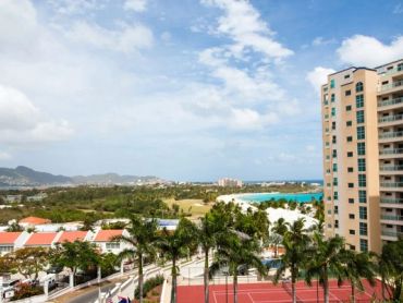 Beachside view with tall buildings and palm trees under a partly cloudy sky.