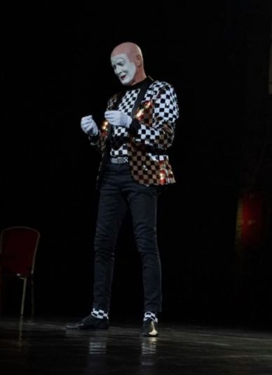 Mime artist in checkered outfit performing on stage.