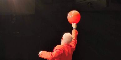 Man in red suit holding a red balloon against a dark background.