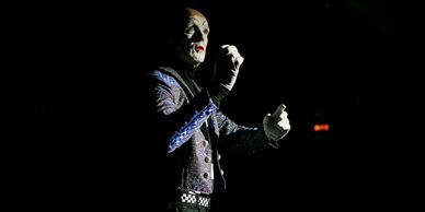 A person dressed as the Joker stands in dramatic lighting against a dark background.