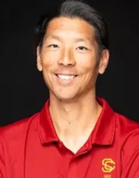 A man wearing a red USC shirt smiling against a black background.