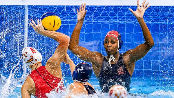 Female water polo players in action near the goal, with a USA goalkeeper ready to block.