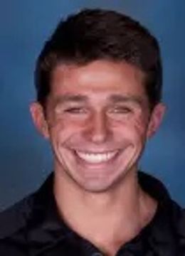 Young man smiling broadly against a blue background.