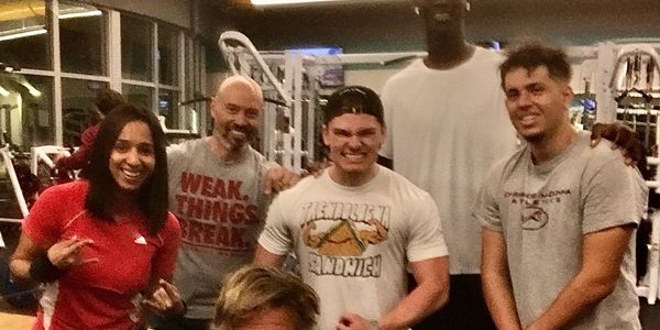 Group of six people posing happily in a gym setting.