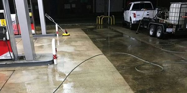 Wet gas station floor with cleaning equipment and a white truck in the background.