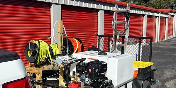 Pressure washing equipment on a trailer in front of red storage unit doors.