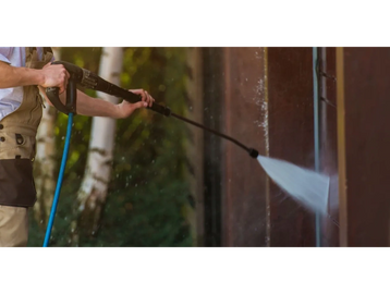 Person pressure washing a dirty wall outdoors.
