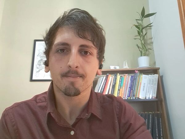 Psicólogo Victor Diaz centralizado e sorrindo. Ao fundo, estante de livros.