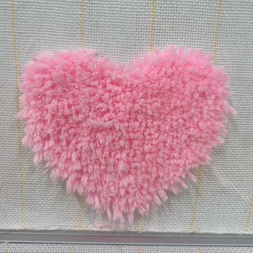 A fluffy pink heart shape on white fabric with yellow grid lines.