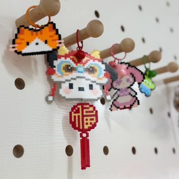Pixel art keychains hanging on wooden hooks on a pegboard wall.