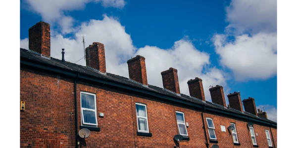 Row of traditional brick terraced houses under a bright blue sky with clouds.