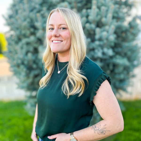 Smiling woman with blonde hair wearing a green top and jeans outdoors.