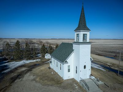 A white church with a tall steeple in a rural landscape.