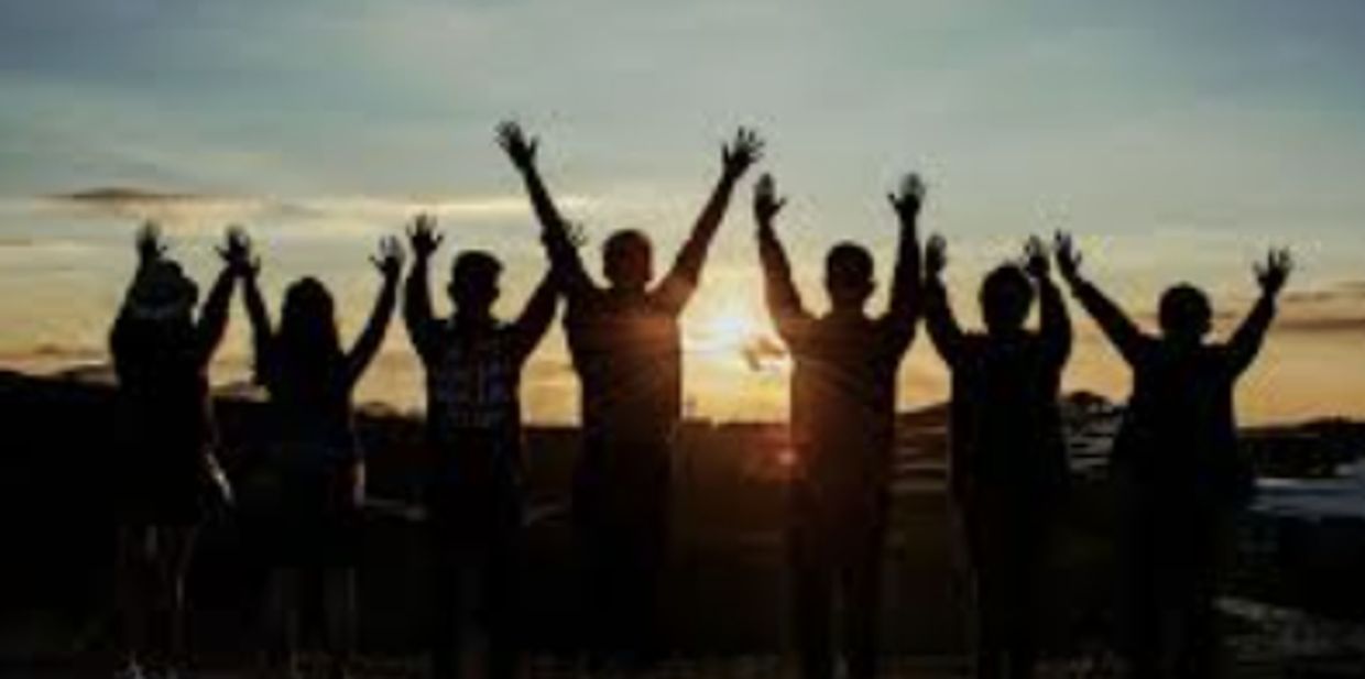 Group of people silhouetted against a sunset with raised hands.