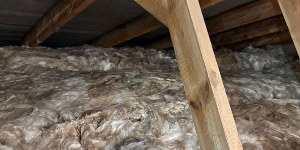 Insulation material installed in an attic under wooden beams.