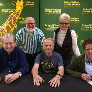 Group of five smiling people at a signing event with a colorful giraffe cutout.
