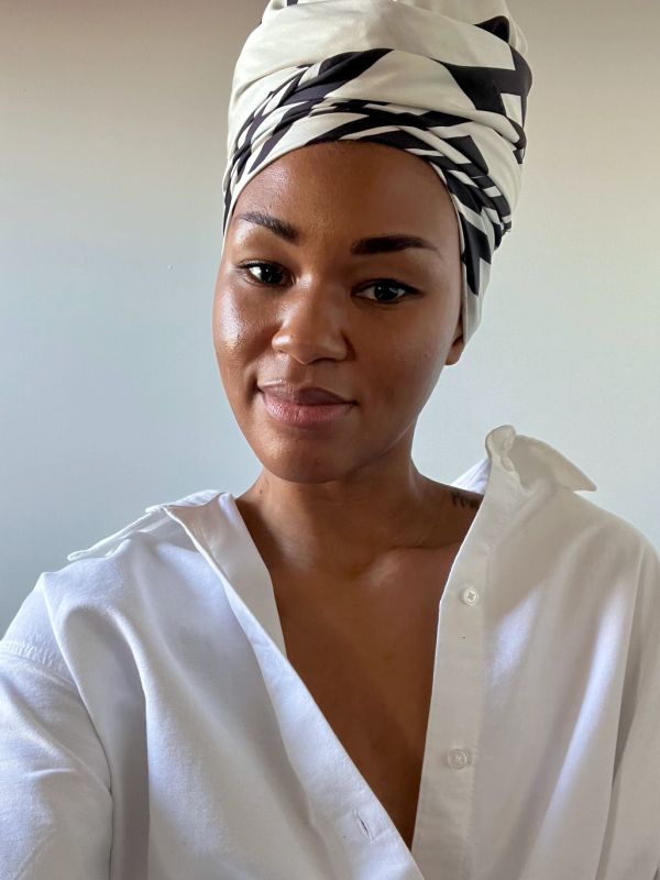 Woman with a white and black headwrap smiling gently.