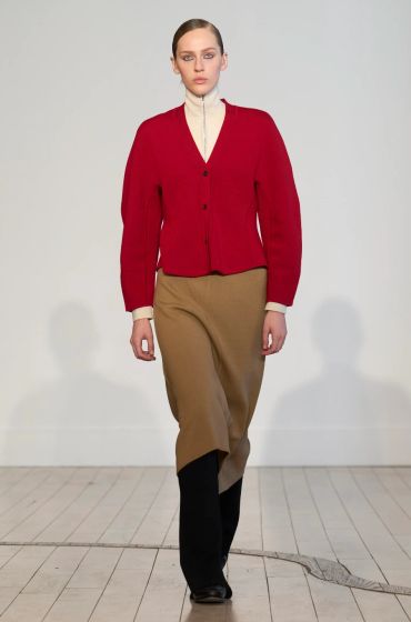 Model wearing a red cardigan and brown skirt with black boots.