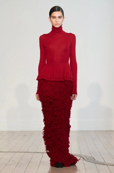 Model in elegant red turtleneck and textured skirt.