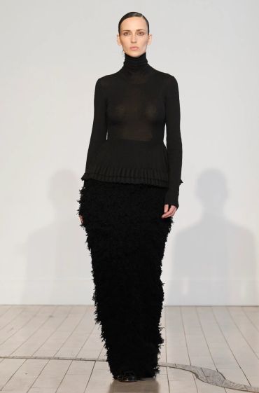 Woman wearing an elegant black outfit with a turtleneck and textured skirt.
