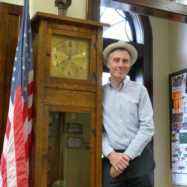 Man smiling next to a grandfather clock and American flag.