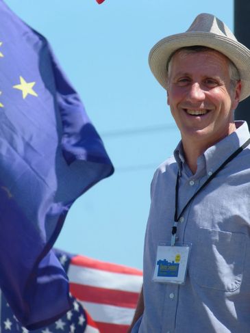 Man smiling with flags in the background.