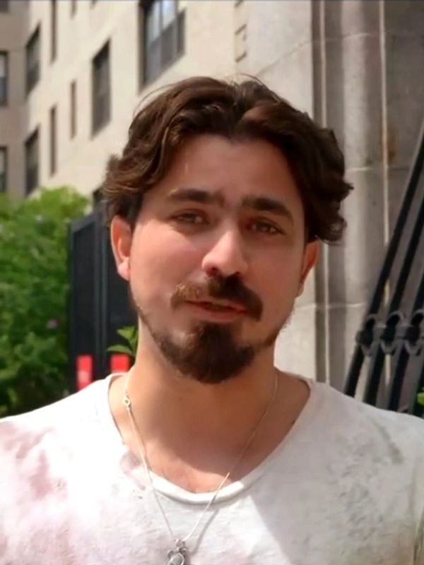 A man with a beard and mustache wearing a white shirt outdoors.