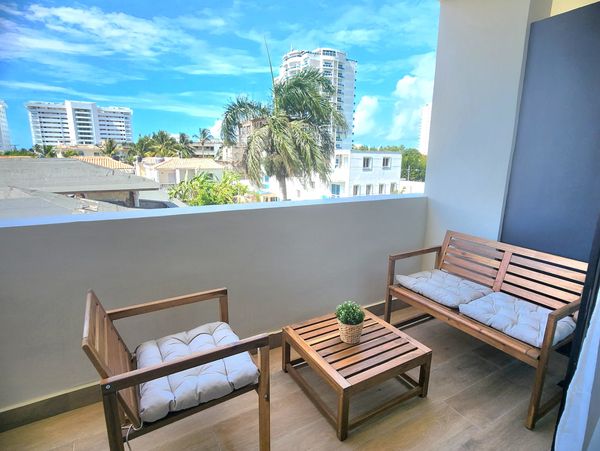 Cozy balcony with wooden furniture and cityscape view under a bright blue sky.