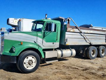 Green dump truck parked on dirt.