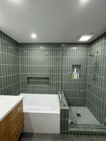 Modern bathroom with green tiled walls, a white bathtub, and a glass-enclosed shower. 2026