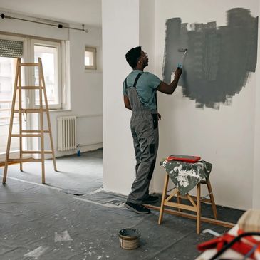 Professional painter applying gray paint to interior wall.