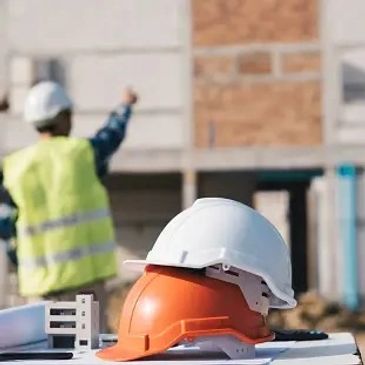 Two construction helmets on a table with a worker in the background.