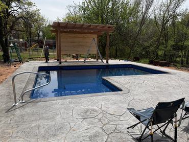 Outdoor pool with concrete deck and pergola in a backyard.