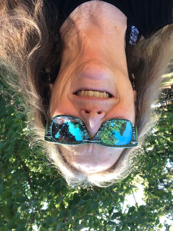 Smiling woman wearing reflective sunglasses with trees reflected in them.