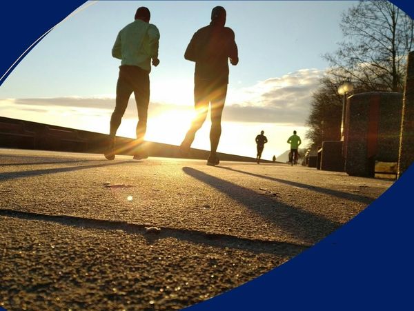 People jogging outdoors during sunrise on a paved path.