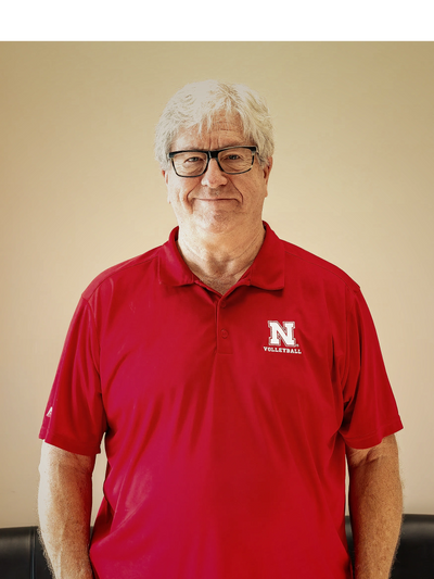 Smiling older man in red Nebraska Volleyball polo shirt with glasses.