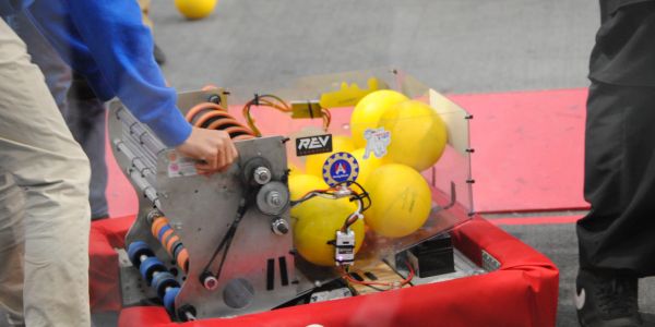 A robot holding yellow balls with two people nearby.