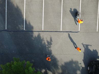 People painting parking lot lines on asphalt from an aerial view.