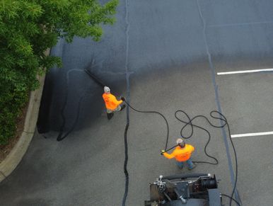 Two workers in orange shirts sealing cracks on an asphalt parking lot.