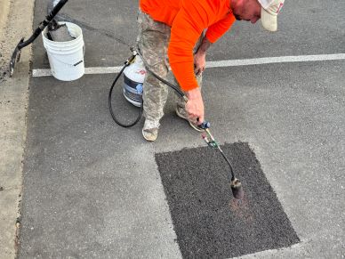 Worker using a torch to seal a freshly patched asphalt road section.