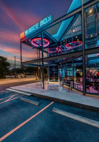 Modern neon-lit building at sunset with reflective glass and vibrant colors.