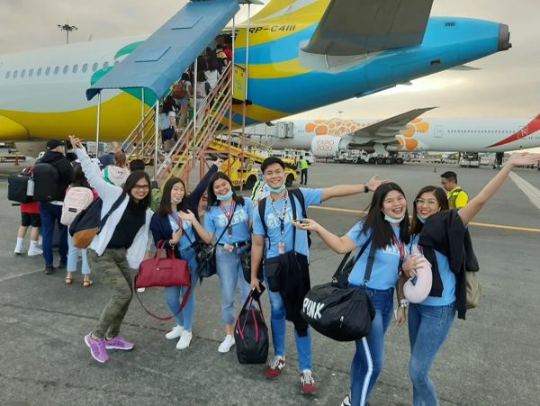 Group of friends posing happily at the airport near a plane.