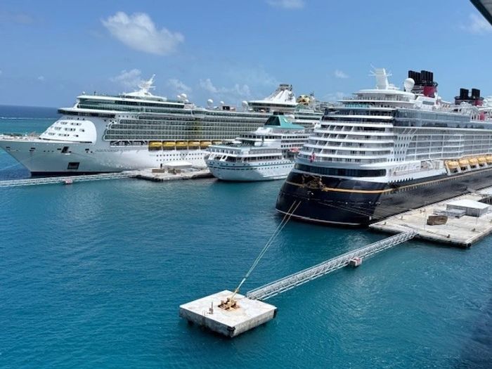 Three large cruise ships docked at a sunny port with clear blue skies.
