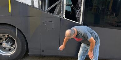 A man inspecting the lower side of a bus with a partially dismantled window.
