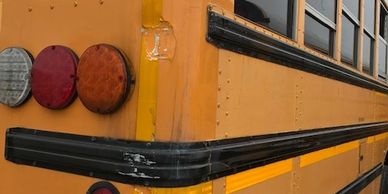 Close-up of the rear side of a yellow school bus with visible wear and scratches.