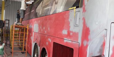 Workers repainting a large bus inside a garage.