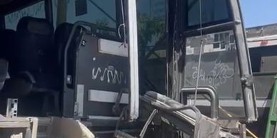 Damaged bus front interior with exposed wiring and torn fabric under clear sky.