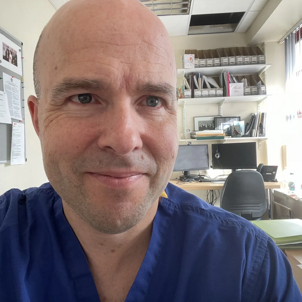 Man in blue scrubs smiling in an office setting.