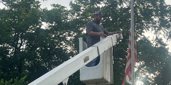 A man in a bucket lift working near an American flag on a pole.